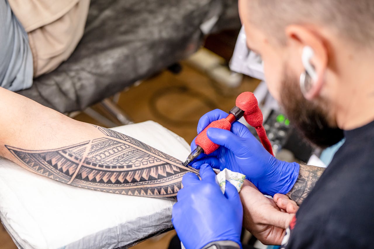 Close-up of a tattoo artist applying intricate design on a client's arm in a studio setting.