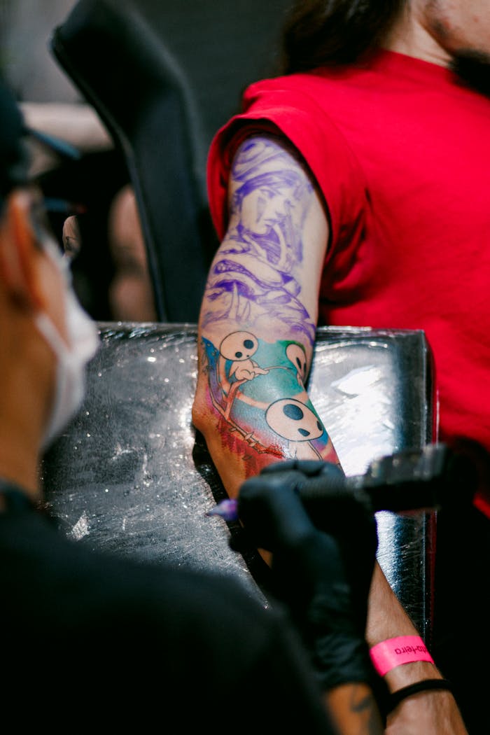 The Art of Drawing Readers In: Your attractive post title goes here Tattoo artist creating a vibrant sleeve tattoo on a client's arm in a modern studio.